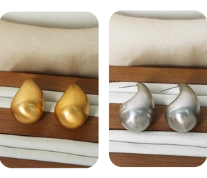 Detailed view of matte teardrop stud earrings in gold and silver finishes on a tray