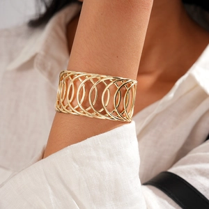 Gros plan d'un large bracelet géométrique doré ajouré porté sur une chemise en lin