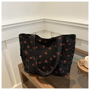 Detail of strawberry pattern on black corduroy tote bag with zipper on wooden table