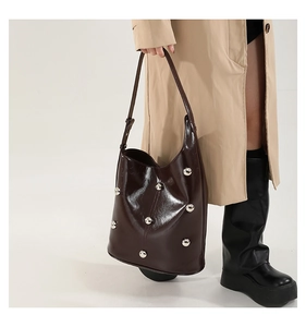 Detail of dark brown patent leather hobo bag with silver studs on model with trench coat