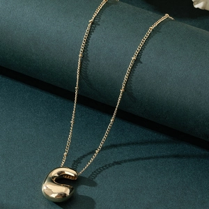 Polished gold balloon letter C pendant necklace with beaded chain on teal background