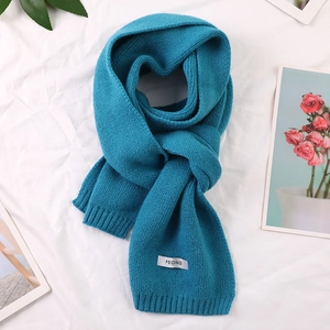 Detail of dark teal knitted scarf with a small white stitched brand label on fabric