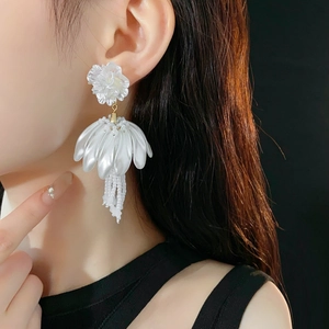 Detailed close-up of white petal crystal tassel earrings on model with black background