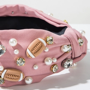 Close-up of knot headband with pearls, rhinestones and football charms on pink fabric