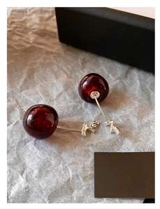 Macro shot of deep red resin cherry pendant earrings on elegant gray texture paper
