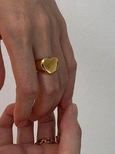 Close-up of golden hollow heart ring and chain-style band on finger with metallic shine