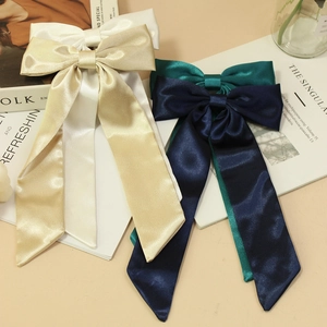 Elegant satin bow hair clip with long ribbons in four classic colors on a beige desk
