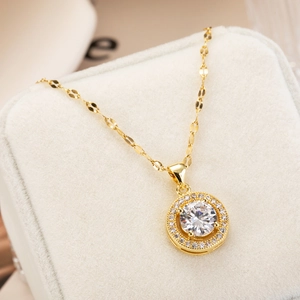 Golden round pendant necklace with sparkling cubic zirconia on a beige jewelry cushion