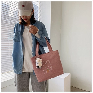 Pink corduroy tote bag detail featuring rabbit embroidery and a spotted cow plush charm