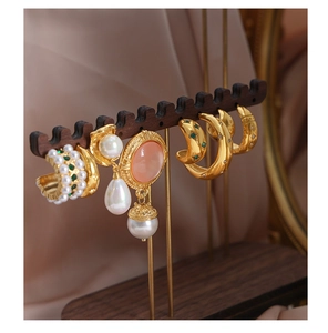 Detail view of gold-plated titanium earrings with zircon and pearls on wood display