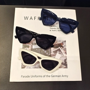 Close-up of stacked cat-eye sunglasses in navy blue, black, and white over vintage books