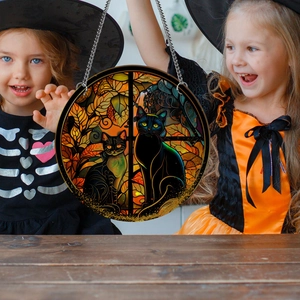 Close-up of Halloween stained glass hanging decor with black cats held by two girls