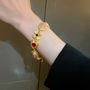 Primer plano de pulsera dorada vintage con camafeo rosa, trébol verde y dije de corazón