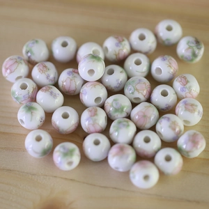 Macro shot of white ceramic beads with floral patterns on light wood background