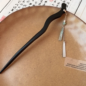 Detail of wave-shaped black ebony hair pin with metallic chain and green bead pendant
