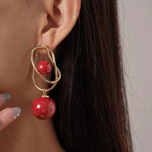 Detail shot of a model wearing geometric gold wire earrings with red spherical beads