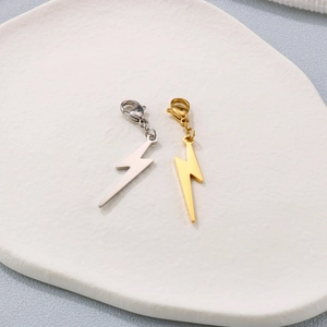Golden and silver lightning bolt pendants with lobster clasps on a ceramic plate