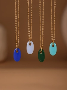 Detail von farbigen ovalen Emaille-Anhängern in Blau, Weiß und Grün an Goldketten