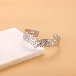 Detail of silver hollow titanium steel cuff bracelet with unique hammered texture on white marble