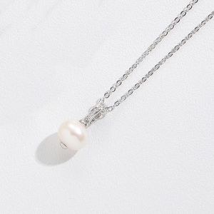 Detail shot of a white pearl necklace with silver chain on white leather background