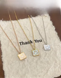 Detail of square smiley face necklaces in gold, silver, and rose gold on a thank you card