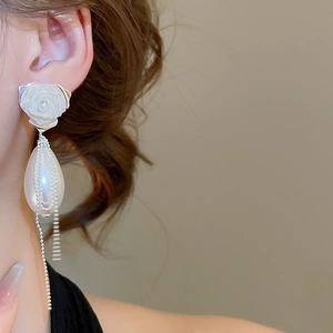 Close-up of rose stud earring with drop pearl and tassel on model's ear