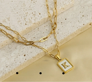 Macro detail of 18K gold paperclip chain and rectangle letter K pendant on silk