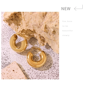 Close-up of chunky gold U-shaped hoop earrings on vintage textured stone background