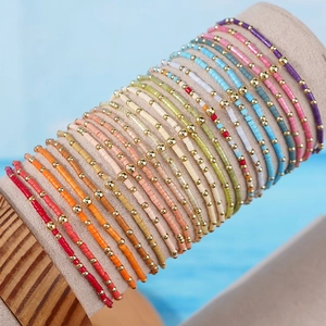 Braccialetti di perline colorate con accenti dorati esposti su un supporto beige per gioielli