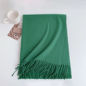 Detail of green cashmere-like scarf showing soft texture and fringe on white surface