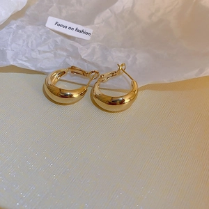 Macro shot of gold chunky hoop earrings with mirror finish on textured beige fabric