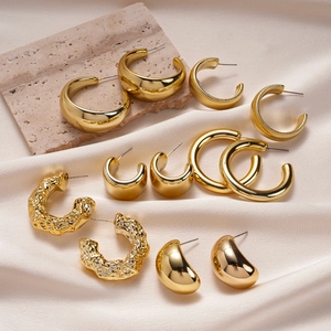 Set of minimalist geometric gold earrings displayed on silk and stone texture background