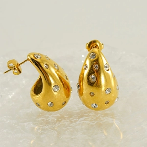 Gros plan de boucles d'oreilles goutte dorées avec cristaux pavés sur verre dépoli