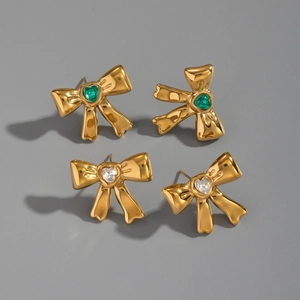 Detail of gold bow earrings featuring green and clear heart zircon stones on gray surface