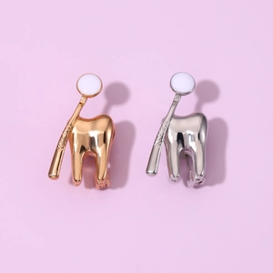 Creative gold and silver tooth with dental mirror metal brooches on purple background