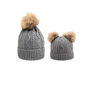 Detail of gray cable-knit parent-child hats with fluffy pom-poms and ribbed cuffs