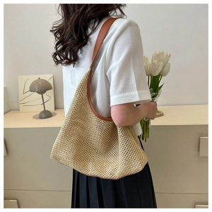 Woven straw tote bag with brown leather trim shown on shoulder in a lifestyle setting
