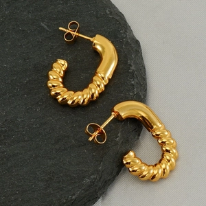 Elegante goldene gedrehte Creolen für Damen auf einem natürlichen grauen Mineralstein