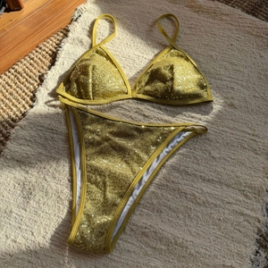 Detail of sequined gold triangle bikini top and high cut bottoms on beige carpet