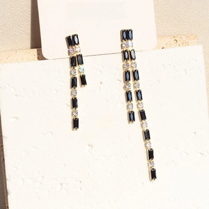 Macro view of asymmetrical gold tassel earrings with black cubic zirconia and diamonds