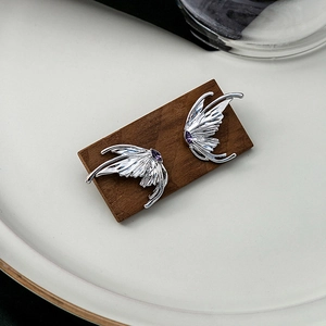 Silver butterfly wing earrings with purple zircon gemstone on a wooden display
