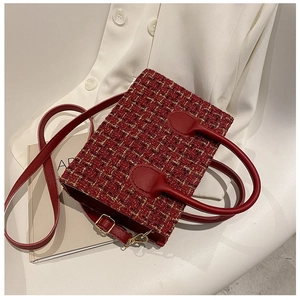 Detailed view of a red tweed handbag with gold threads and leather handle on a white shirt