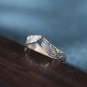 Adjustable sterling silver angel wing ring with intricate feather texture on dark wood