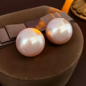 Detailed view of large pinkish pearl stud earrings on a dark brown velvet jewelry box