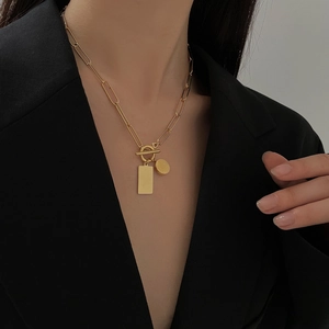 Detail of gold paperclip chain necklace with T-bar clasp and square pendant on model