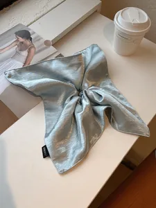 Detailed view of large ice blue satin scrunchie with Hand Made label on a stylish desk