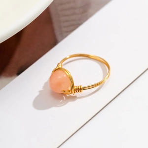 Detail of handmade gold wire-wrapped ring with a translucent pink-orange gemstone bead