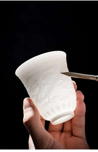 Detail of translucent white jade porcelain cup featuring relief dragon and cloud carvings