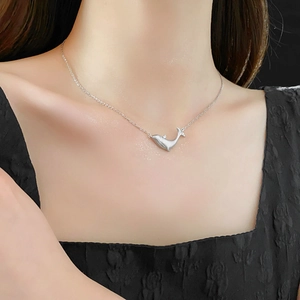 Elegant silver whale pendant necklace shown on a model against a black dress backdrop