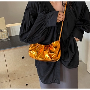 Detail showing metallic orange pleated cloud bag with shiny texture and thin strap